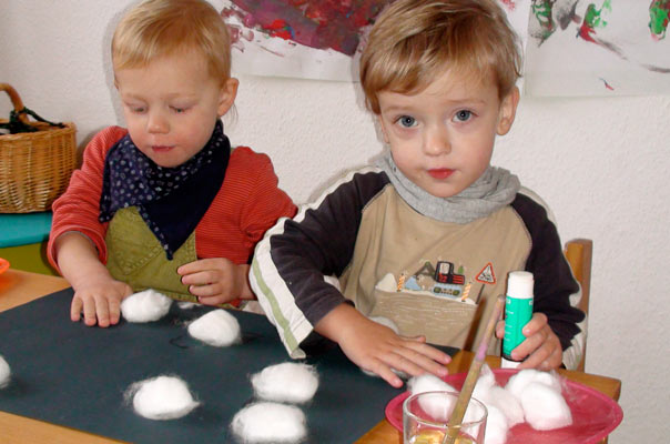 Tageskinder in der Kindertagespflege basteln Schneeflocken aus Watte und Kartoffeldruck.